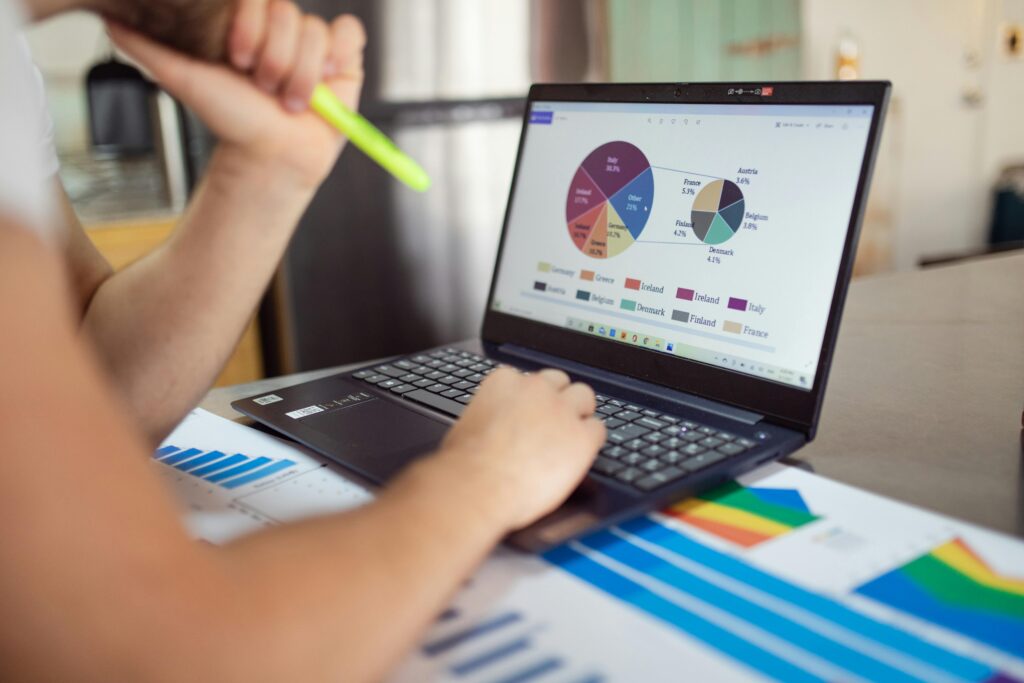 Home Person analyzing financial charts and graphs on a laptop with colorful documents, showcasing market analysis.
